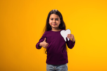 Child girl holding papercraft tooth and showing thumb up gesture over yellow background. Dental...