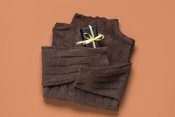 Stylish sweater with gift box on brown background