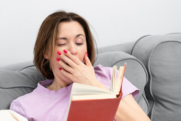 Young attractive sleepy woman yawning while reading book