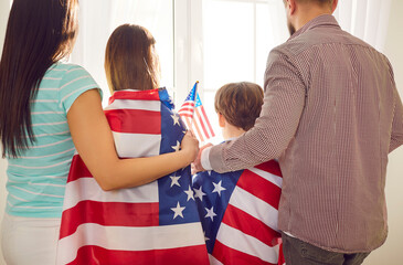 An American family, draped in USA flags, joyfully celebrates Independence Day at home. The backside...