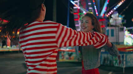 Naklejka premium Closeup happy girls dance city funfair at night. Cheerful best friends have fun