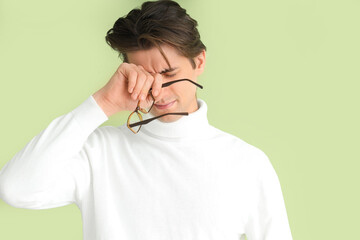 Tired young man with eyeglasses on green background. Glaucoma awareness month