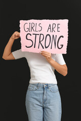 Woman covering face with sign GIRLS ARE STRONG on black background. Feminism concept