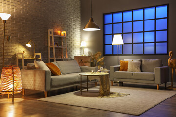 Interior of stylish living room with golden decor, glowing lamps and sofas at night