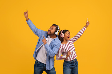 Happy young black couple wearing headphones enjoying music and dancing together