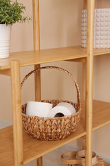 Wicker basket with rolls of toilet paper on wooden shelf in bathroom