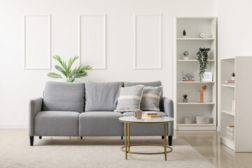 Interior of light living room with grey sofa, table and shelf units