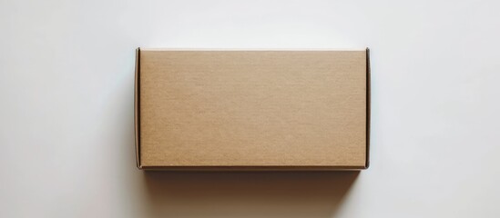 Fototapeta premium A brown cardboard box is seen placed on top of a clean, white wall. The box is rectangular and stands out against the plain background.