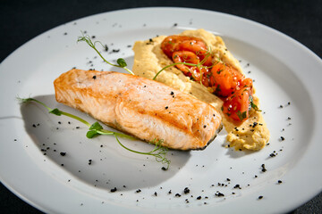 Close-up of salmon steak with hummus and tomatoes on a white plate