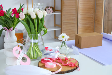 Obraz na płótnie Canvas Gift box, packing materials and tulip flowers on light table. Woman with gift box, packing materials and beautiful tulip flowers at light table in room. International Women's Day