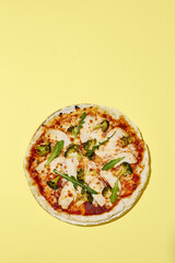 Top view of a gluten-free pizza with turkey and broccoli on a bright yellow surface