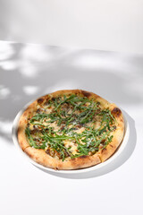 Italian pizza with cheese and mushrooms, adorned with arugula and cast in shadow on a white background