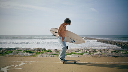 Young man surfer skateboarding on road near beautiful summer ocean close up.  - obrazy, fototapety, plakaty