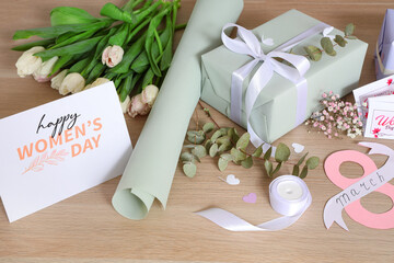 Beautiful gift box, packing materials, flowers and greeting card for International Women's Day on wooden background