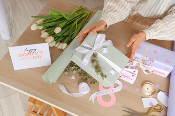 Female hands with gift boxes, packing materials and beautiful flowers at wooden table....