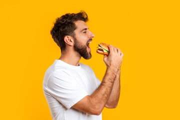 Side View Of Hungry Man Biting Big Burger In Studio