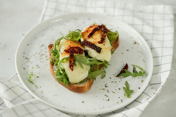 Toast with grilled cheese on bread with salad ans sun dried tomatoes perfect for breakfast and easy to cook on white marble background close up selective focus