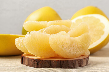 Wooden board with sweet pomelo pieces on light background