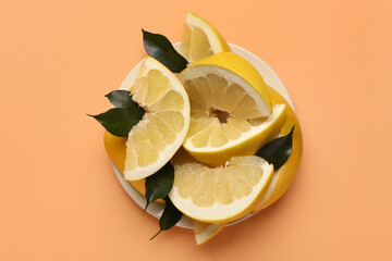 Plate with sweet pomelo slices and leaves on orange background
