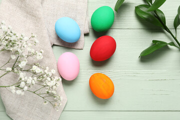 Painted Easter eggs with cloth, flowers and green branch on wooden background