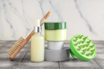 Plaster podiums with silicone head massage brush and cosmetic products on grey tile table against white grunge background