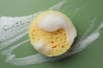 Yellow sponge with foam on green background, top view