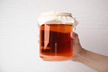 Woman holding glass jar of tasty kombucha on white background, closeup