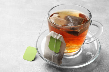 Tea bags and glass cup of hot beverage on light table, closeup. Space for text