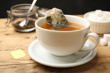 Tea brewing. White cup with tea bag on wooden table, closeup