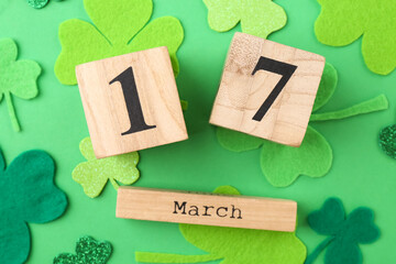 St. Patrick's day - 17th of March. Block calendar and decorative clover leaves on green background, flat lay