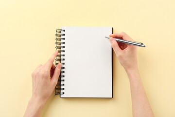 Woman writing in notebook on beige background, top view