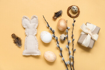 Painted Easter eggs with pussy willow branches, toy bunny and gift box on beige background
