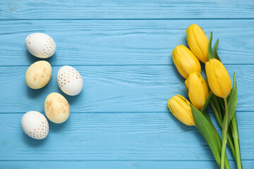 Beautiful tulip flowers with painted Easter eggs on blue wooden background
