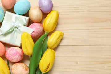 Beautiful tulip flowers with painted Easter eggs and gift box on light wooden background