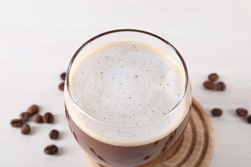 Refreshing iced coffee with milk in glass and beans on white table, closeup