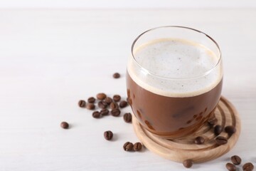 Refreshing iced coffee with milk in glass and beans on white table, closeup. Space for text