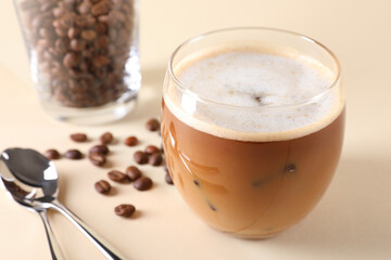 Refreshing iced coffee with milk in glass, beans and spoons on beige table, closeup