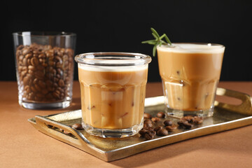 Refreshing iced coffee with milk in glasses and beans on brown table