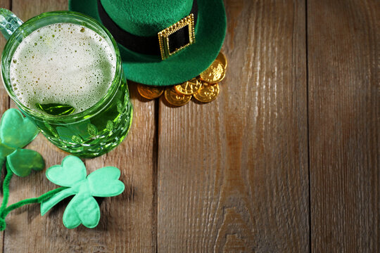 St. Patrick's day party. Green beer, leprechaun hat, gold and decorative clover leaves on wooden table, above view. Space for text