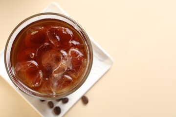 Refreshing iced coffee in glass on beige table, top view. Space for text