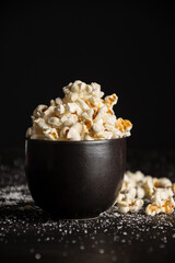 Closeup of black bowl with popcorn on dark table with salt , selective focus, black background,...