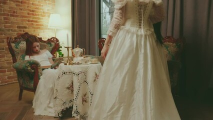 Happy woman queen and friends maids of honor communicate talk. noble lady girl princess sitting on sofa have fun tea party in living room royal family together. Ball gown white vintage dress old style