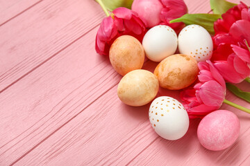 Painted Easter eggs and beautiful tulip flowers on pink wooden background