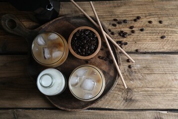 Refreshing iced coffee with milk in glasses, ingredients and straws on wooden table, flat lay. Space for text