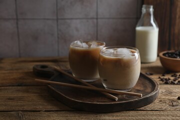 Refreshing iced coffee with milk in glasses and straws on wooden table