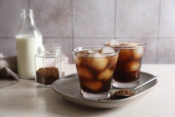 Refreshing iced coffee with milk in glasses, ingredients and spoon on light table