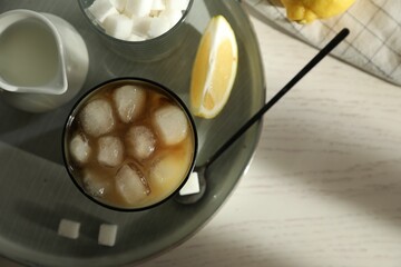 Refreshing iced coffee with milk in glass, sugar cubes and spoon on white wooden table, top view. Space for text
