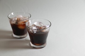 Refreshing iced coffee in glasses on grey background. Space for text