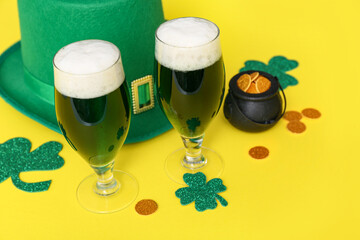 Glasses of beer with clover, coins and leprechaun hat on yellow background. St. Patrick's Day celebration