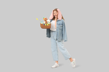 Beautiful young happy woman in bunny ears with Easter basket on grey background